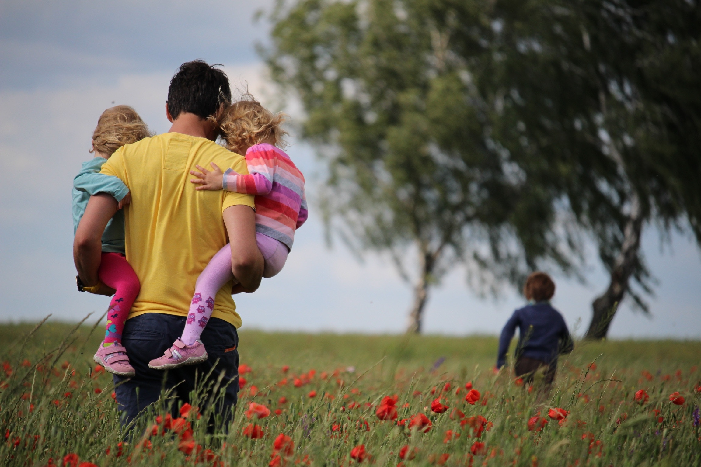 an adult carrying two children in their arms as they walk through a field of flowers