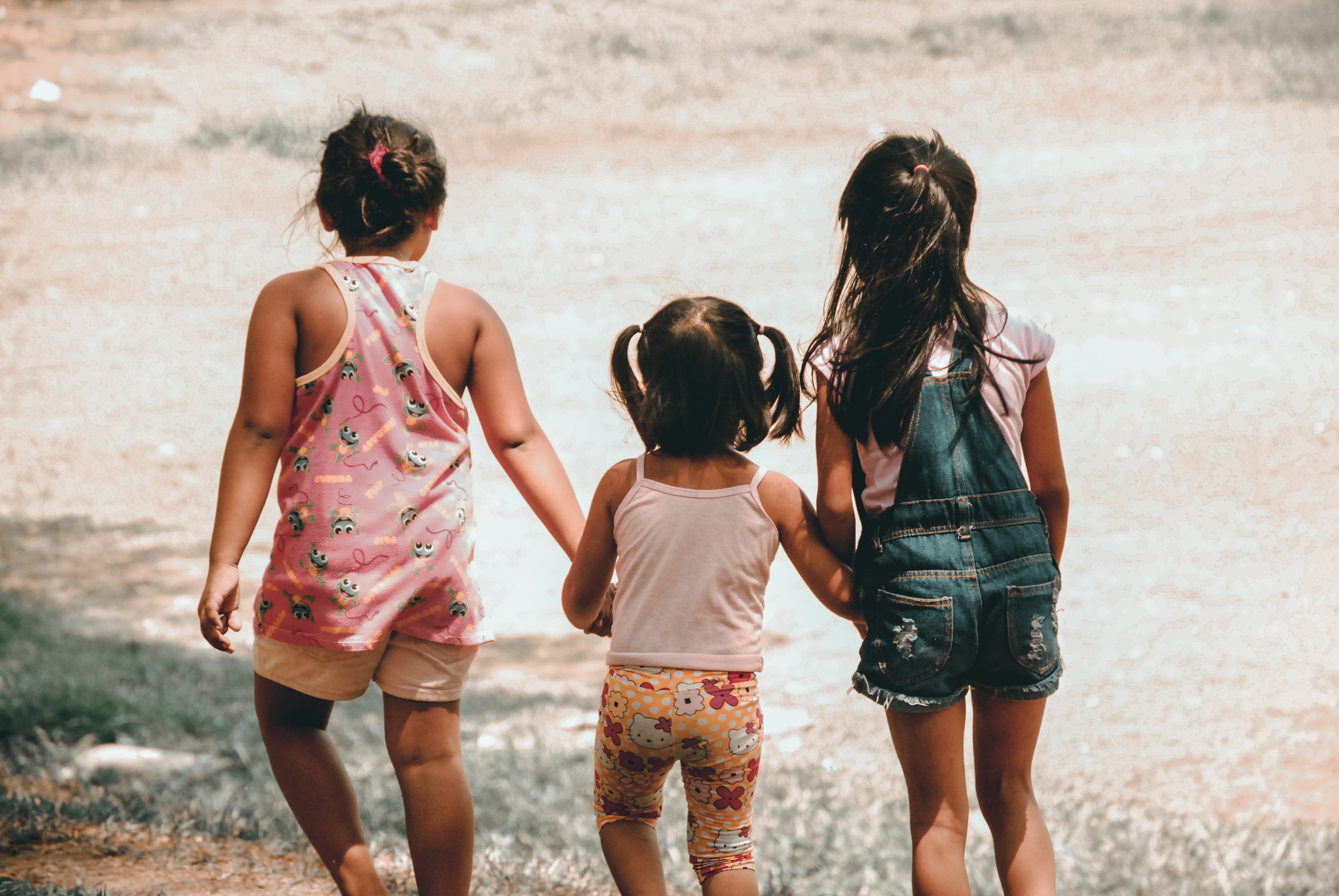Three kids holding hands while looking out at the tide on a beach