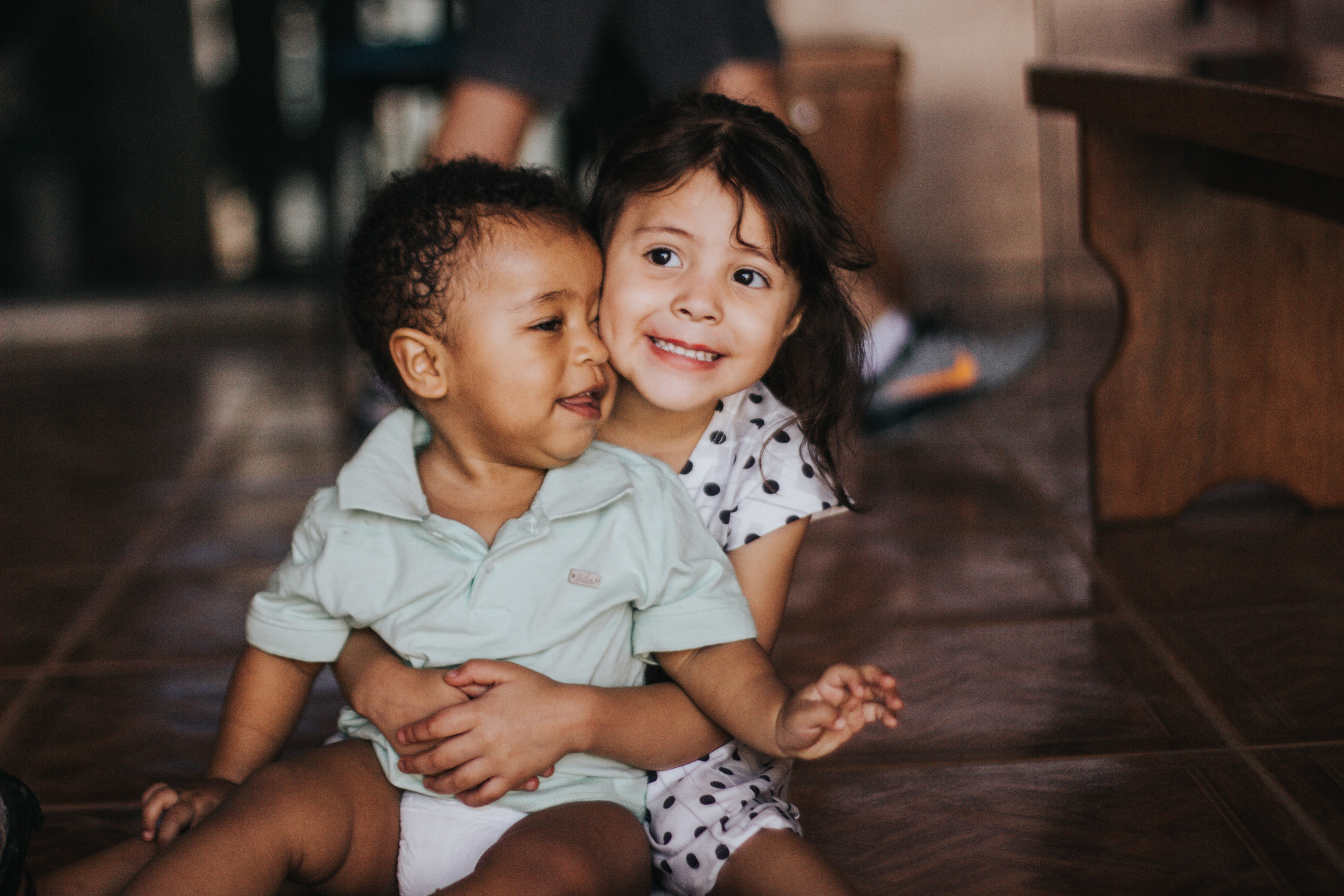 An older girl with a younger boy sitting on her lap, with her arms wrapped around him 