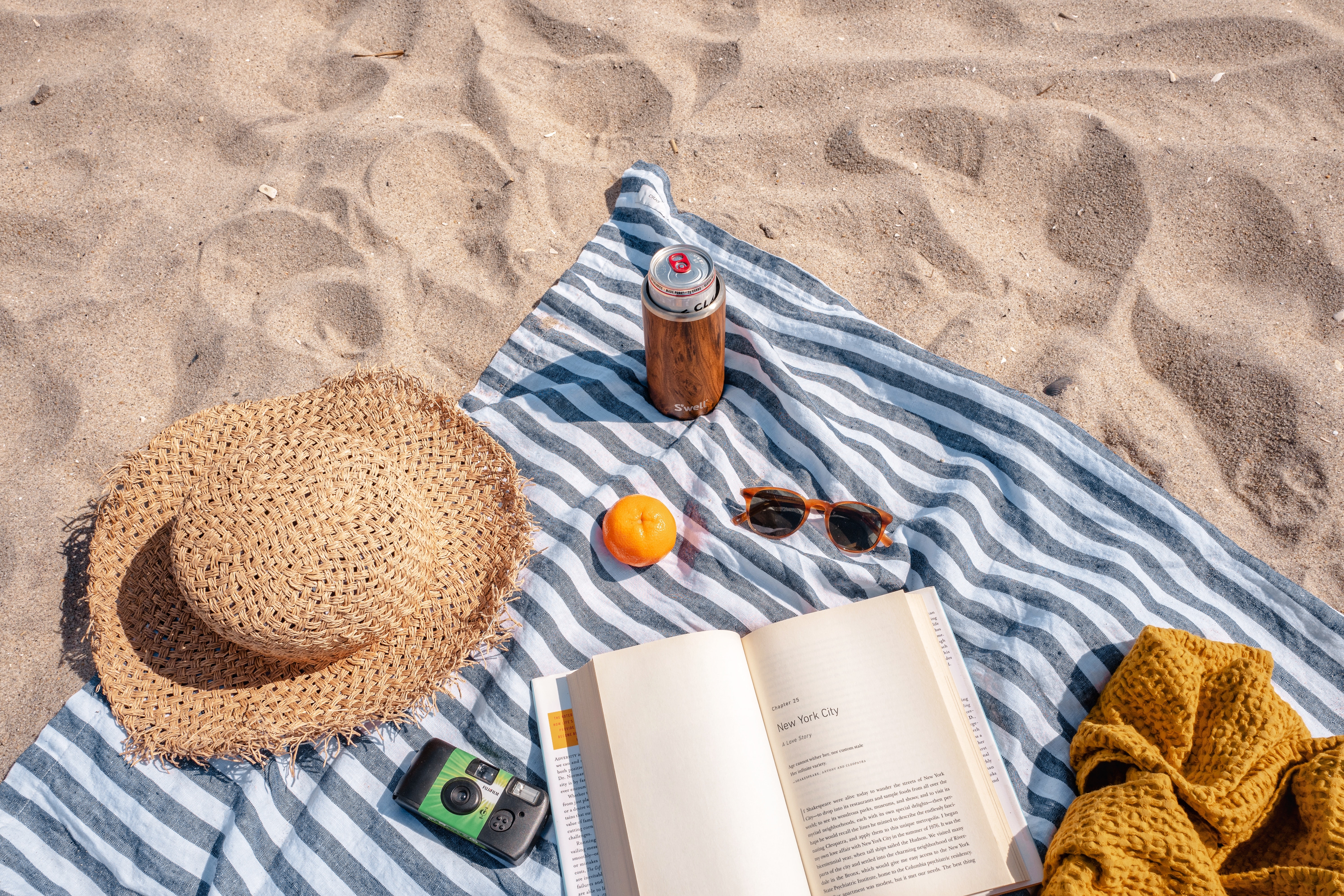 A towel, book, snack and drink on a beach