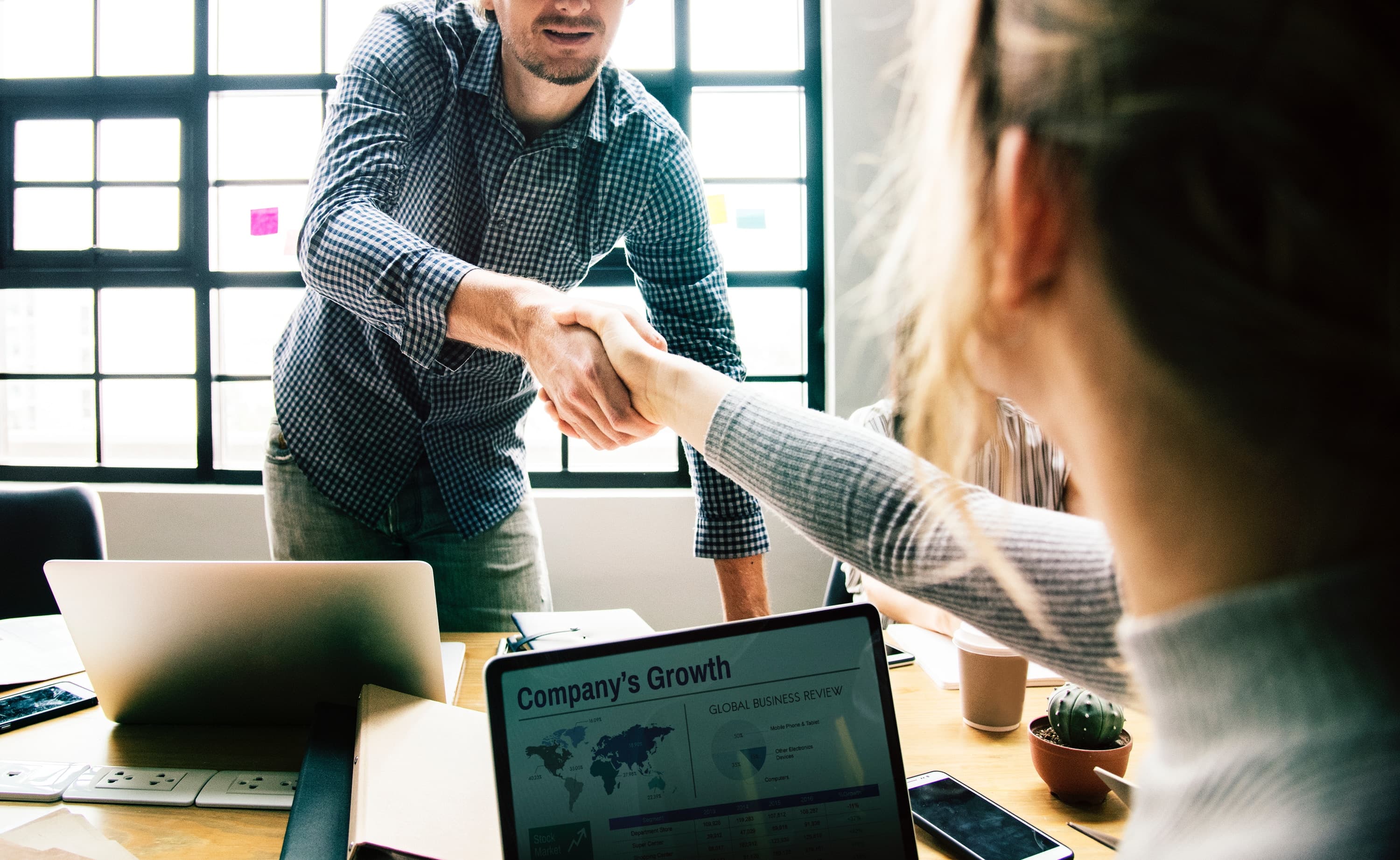 Woman sitting at a desk, shaking the hand of a man standing up, as he's ready to sit down for an interview