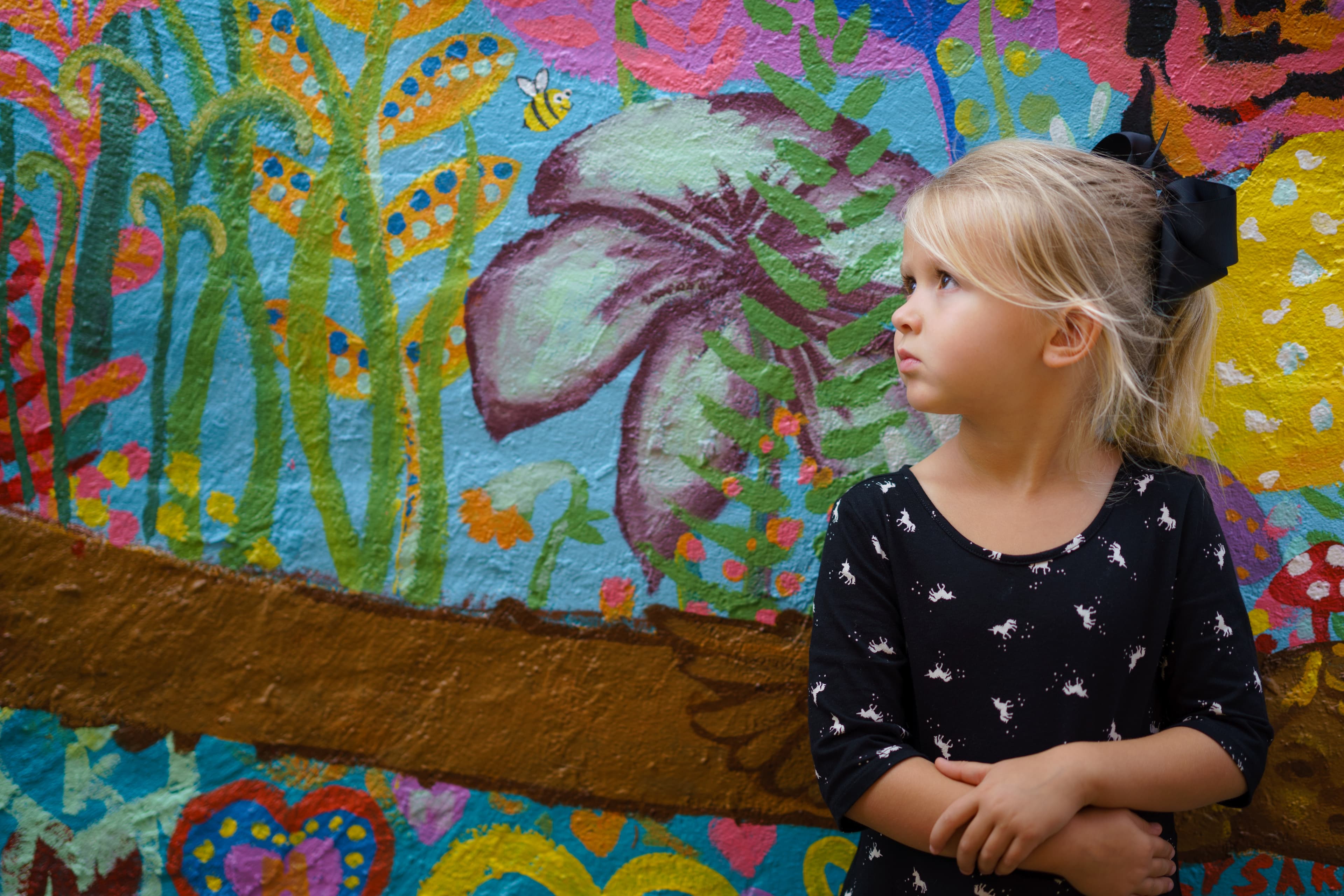 A young girl posing in front of a wall painted with a colorful flower