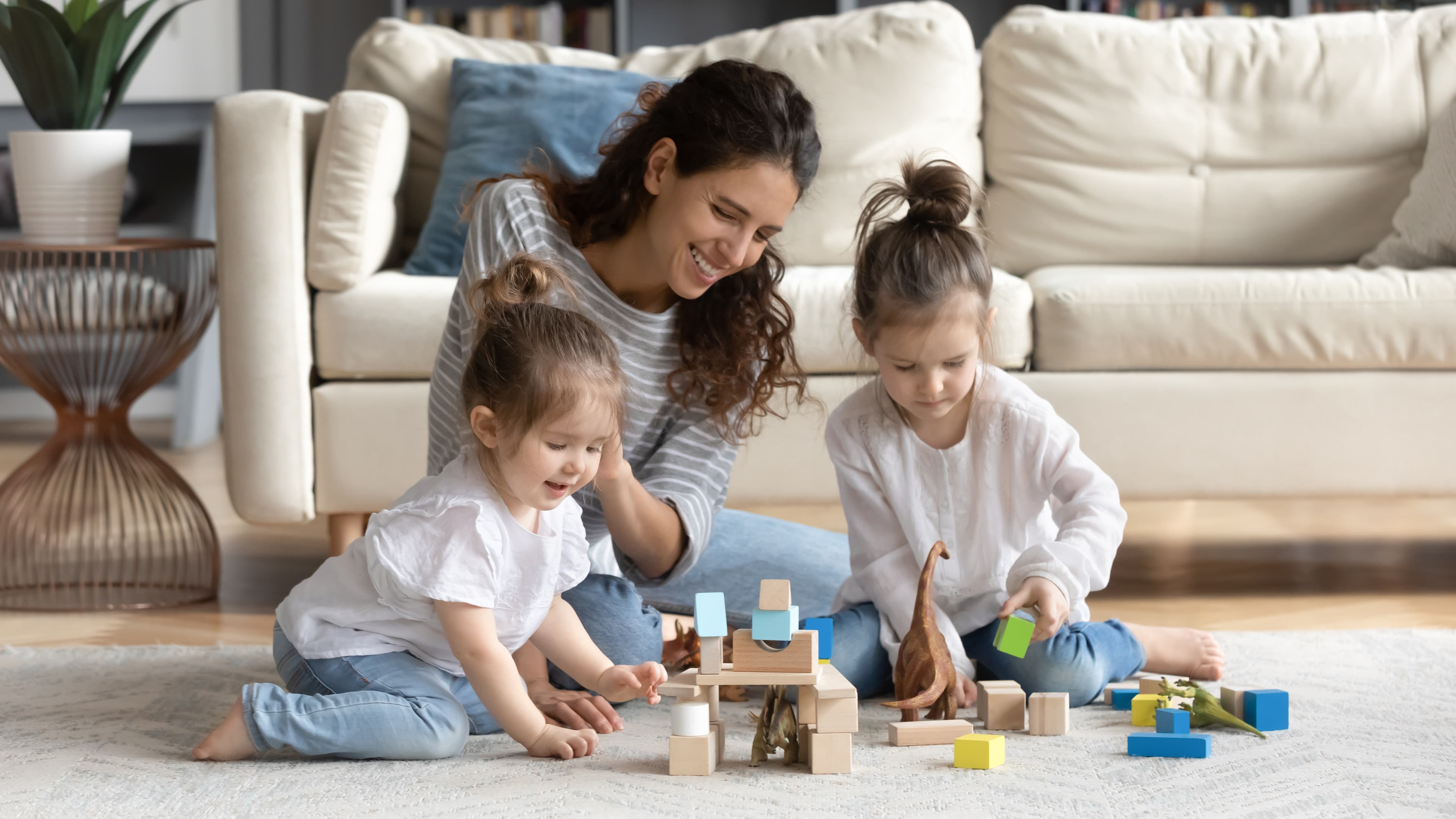 a woman and two children sitting on the floor in front of a sofa in a living room. They are playing with alphabet blocks.