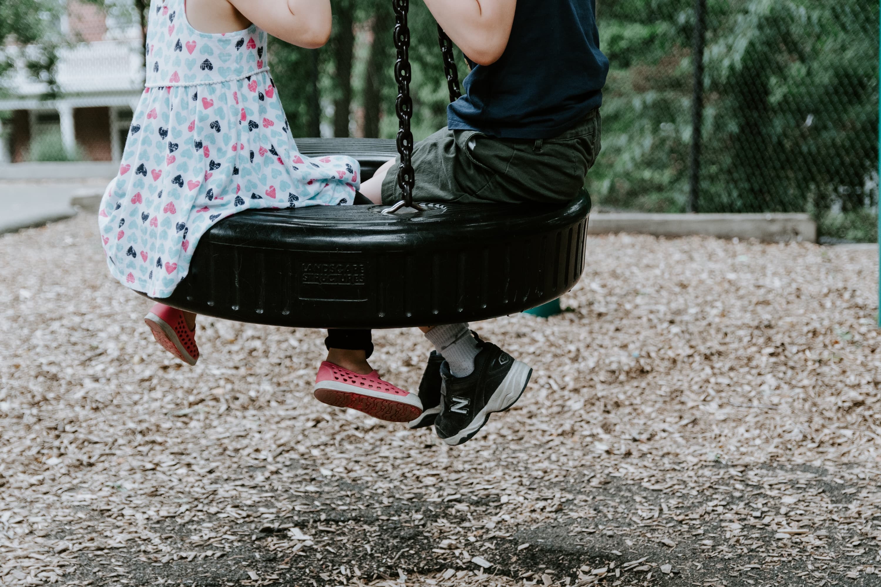 A boy and a girl sitting on a tire swing that is hanging