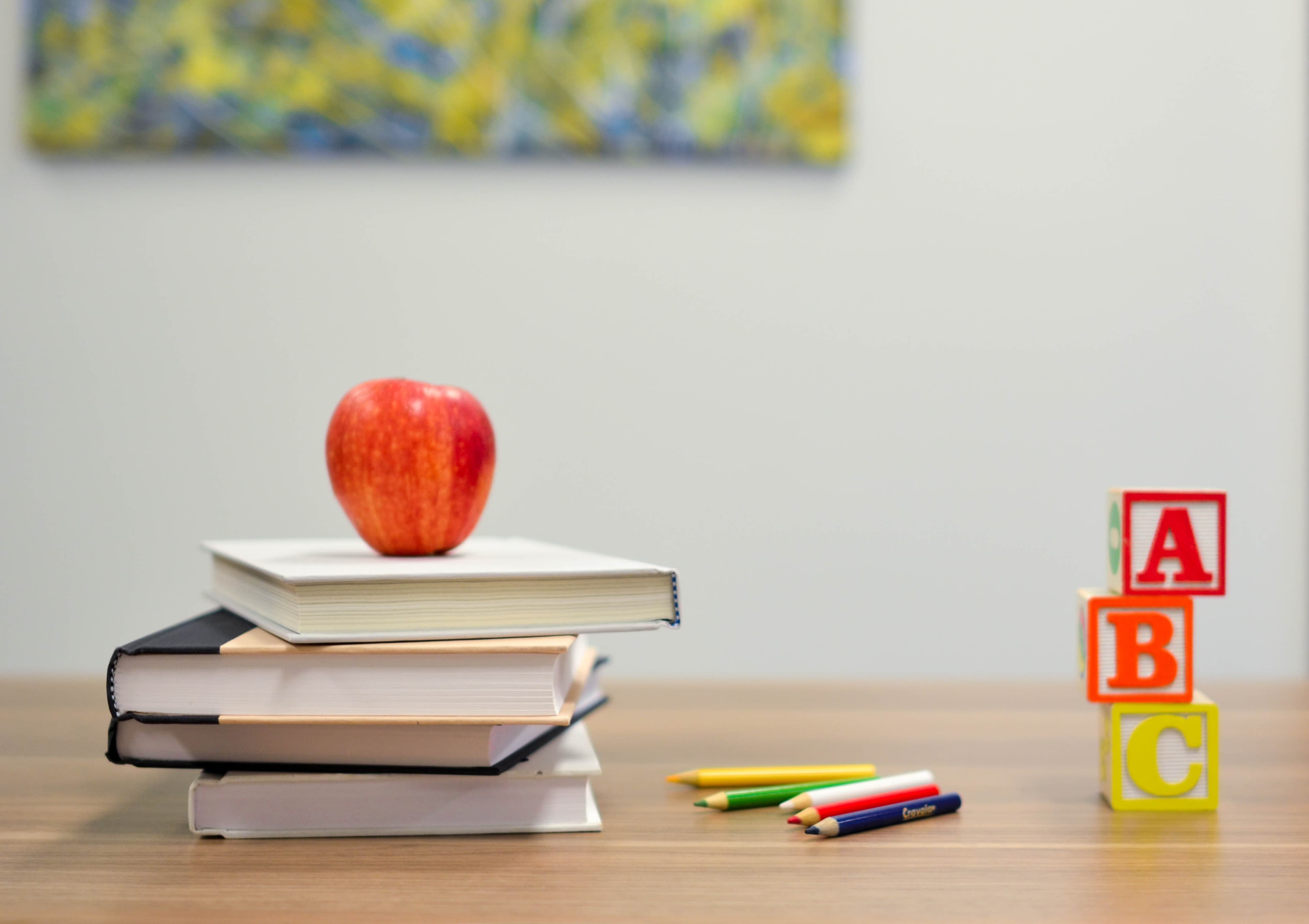 An apple with a pile of colorful books resting upon a wooden desk